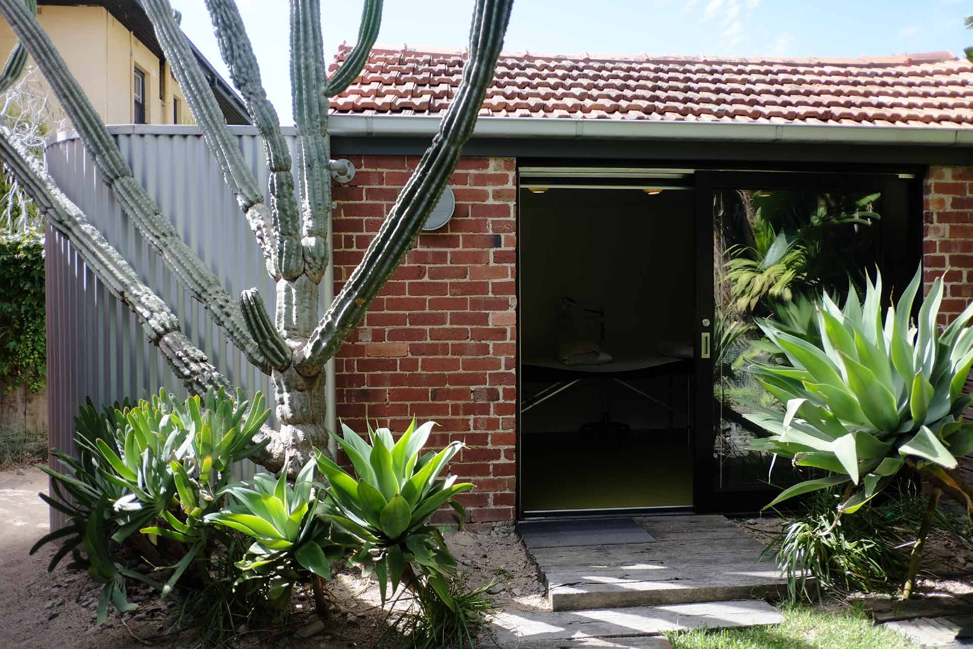 Brick garage with open door flanked by succulent plants and an acupuncture-like tall cactus, reminiscent of Chinese Medicine.