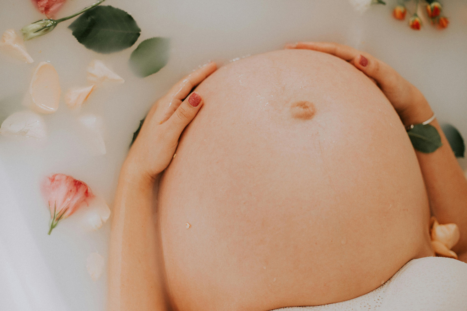 A pregnant person relaxing in a bath with floral petals, exploring Chinese Medicine for fertility.